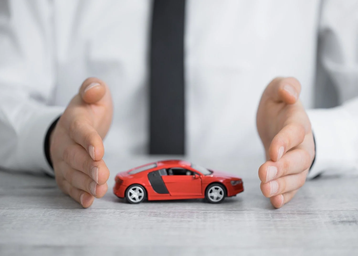 Two hands held protectively around a small red model car